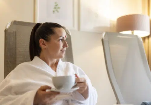 Ihr seht eine Frau, die sich nach einer Behandlung im Tulsi Ayurveda-Zentrum im JUFA Hotel Stift Gurk**** bei einem Tee im Wellnessbereich entspannt. Der Ort für erholsamen Thermen- und entspannten Wellnessurlaub für die ganze Familie.