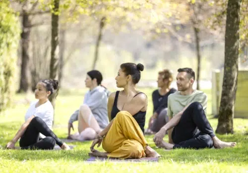 Ihr seht eine Gruppe, die an einer outdoor Yoga Session im Klostergarten des JUFA Hotel Stift Gurk**** teilnimmt. Der Ort für erholsamen Thermen- und entspannten Wellnessurlaub für die ganze Familie.