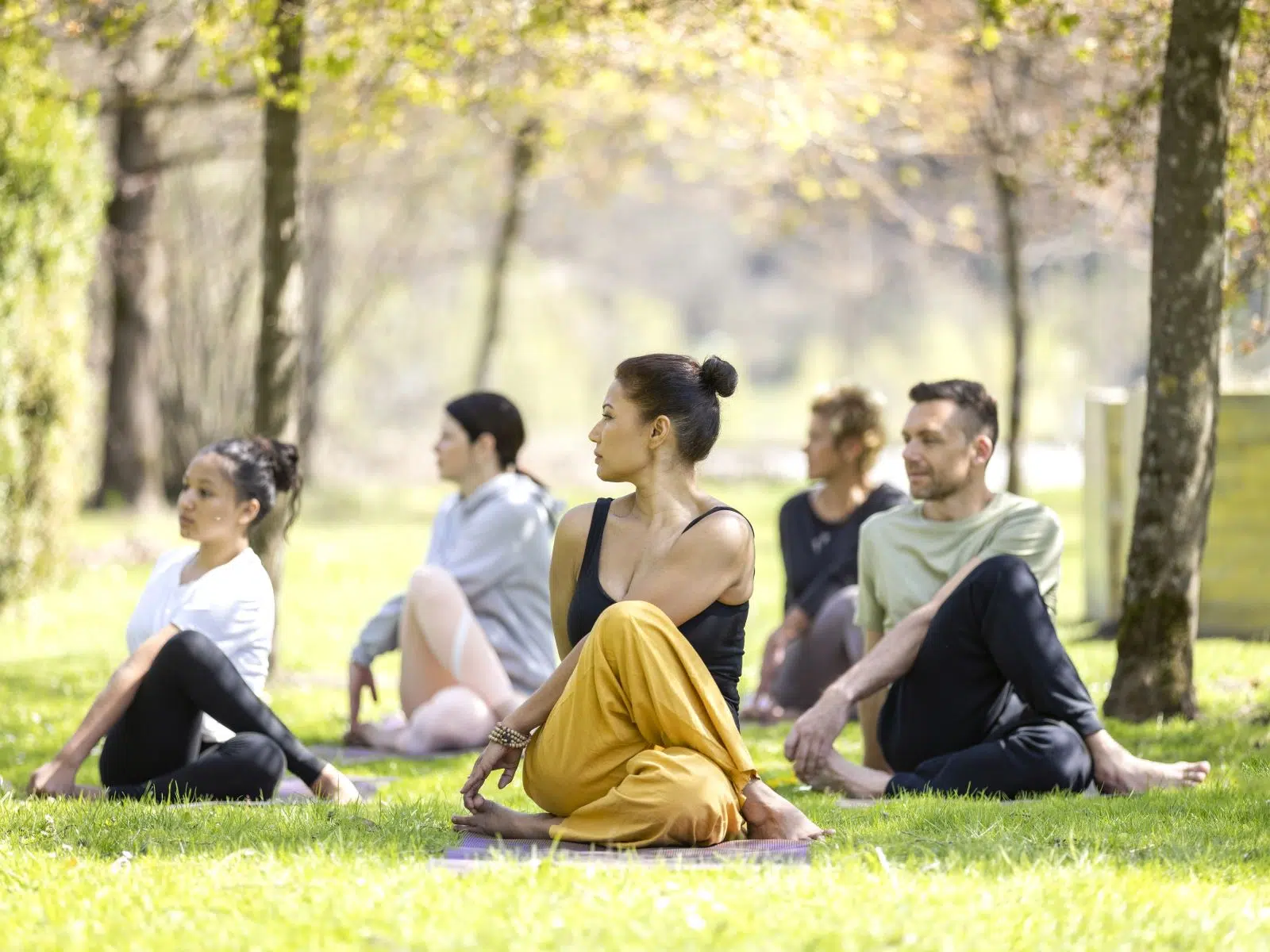 Ihr seht eine Gruppe, die an einer outdoor Yoga Session im Klostergarten des JUFA Hotel Stift Gurk**** teilnimmt. Der Ort für erholsamen Thermen- und entspannten Wellnessurlaub für die ganze Familie.