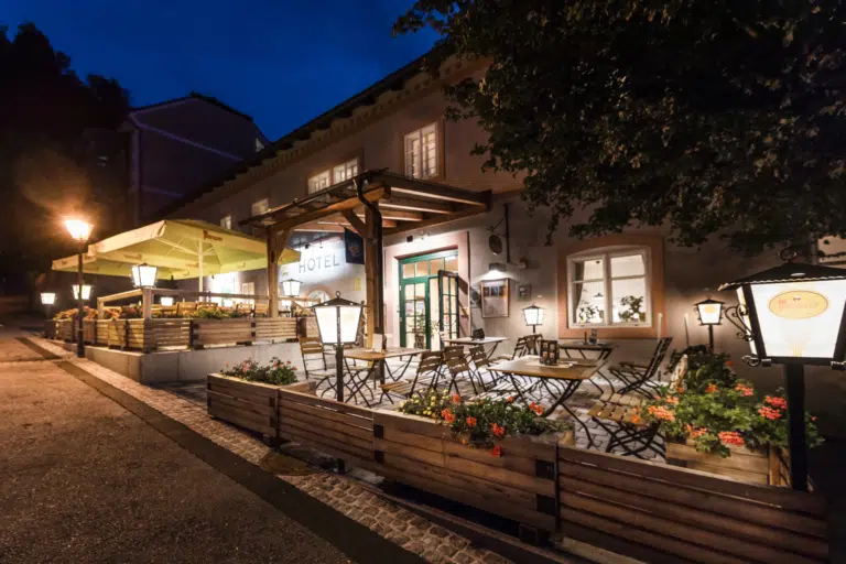 Ihr seht eine Außenansicht mit Hoteleingang und Gastgarten vom JUFA Hotel Murau am Abend. JUFA Hotels bietet erholsamen Familienurlaub und einen unvergesslichen Winter- und Wanderurlaub.