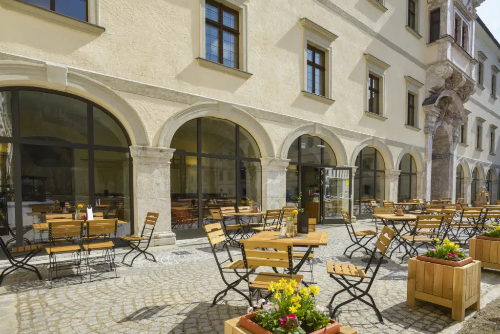 Ihr seht den Innenhof mit Terrasse, Gartenmöbel und Fensterfront im Hintergrund im JUFA Hotel Spital am Pyhrn.