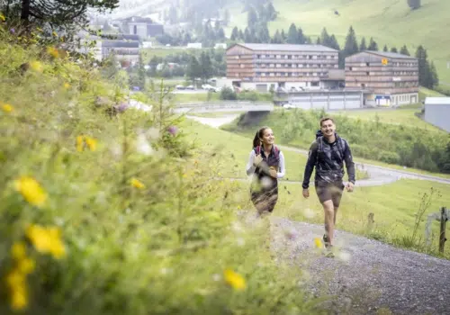 Ihr seht ein Paar beim Wandern vor dem JUFA Hotel Malbun.