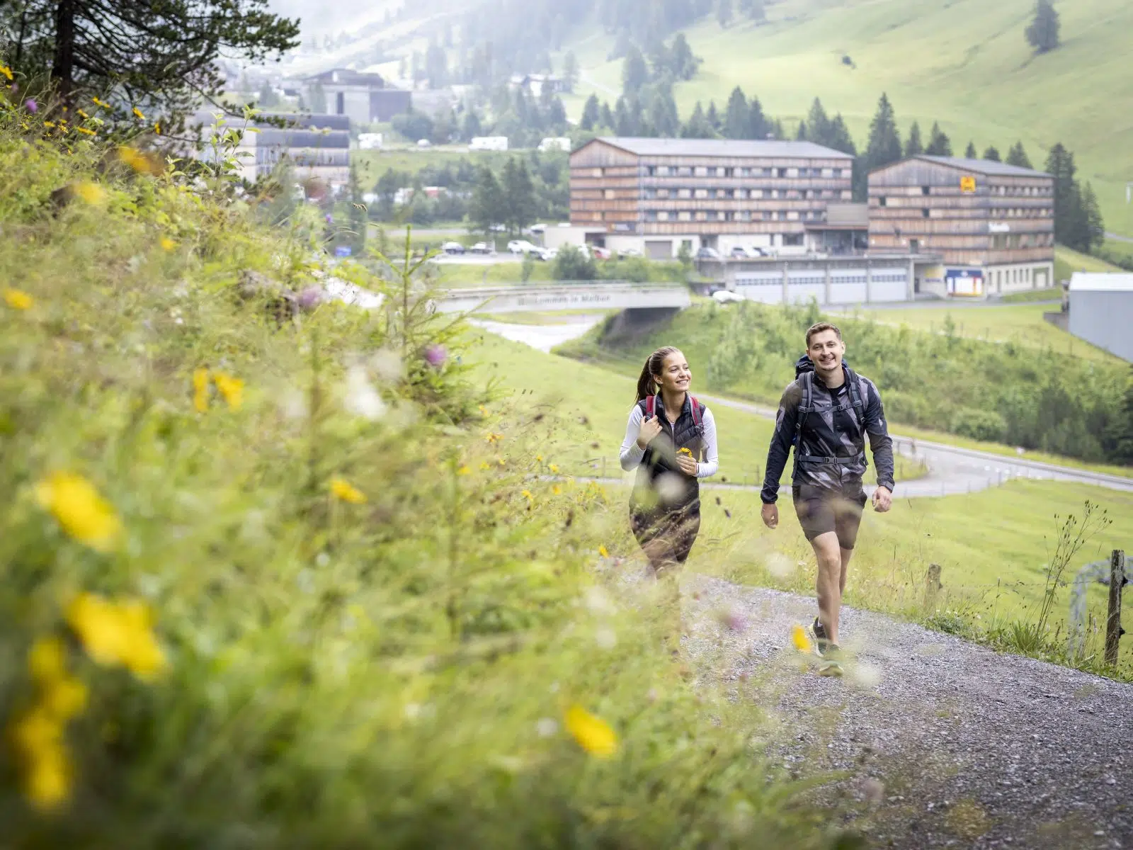 Ihr seht ein Paar beim Wandern vor dem JUFA Hotel Malbun.