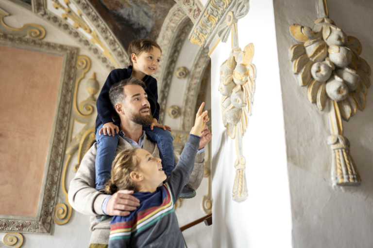 Ihr seht einen Vater mit seinen beiden Kindern. Die Tochter und der Vater zeigen auf das Wandrelief aus Stein im Museum Murtal. JUFA Hotels bietet kinderfreundlichen und erlebnisreichen Urlaub für die ganze Familie.