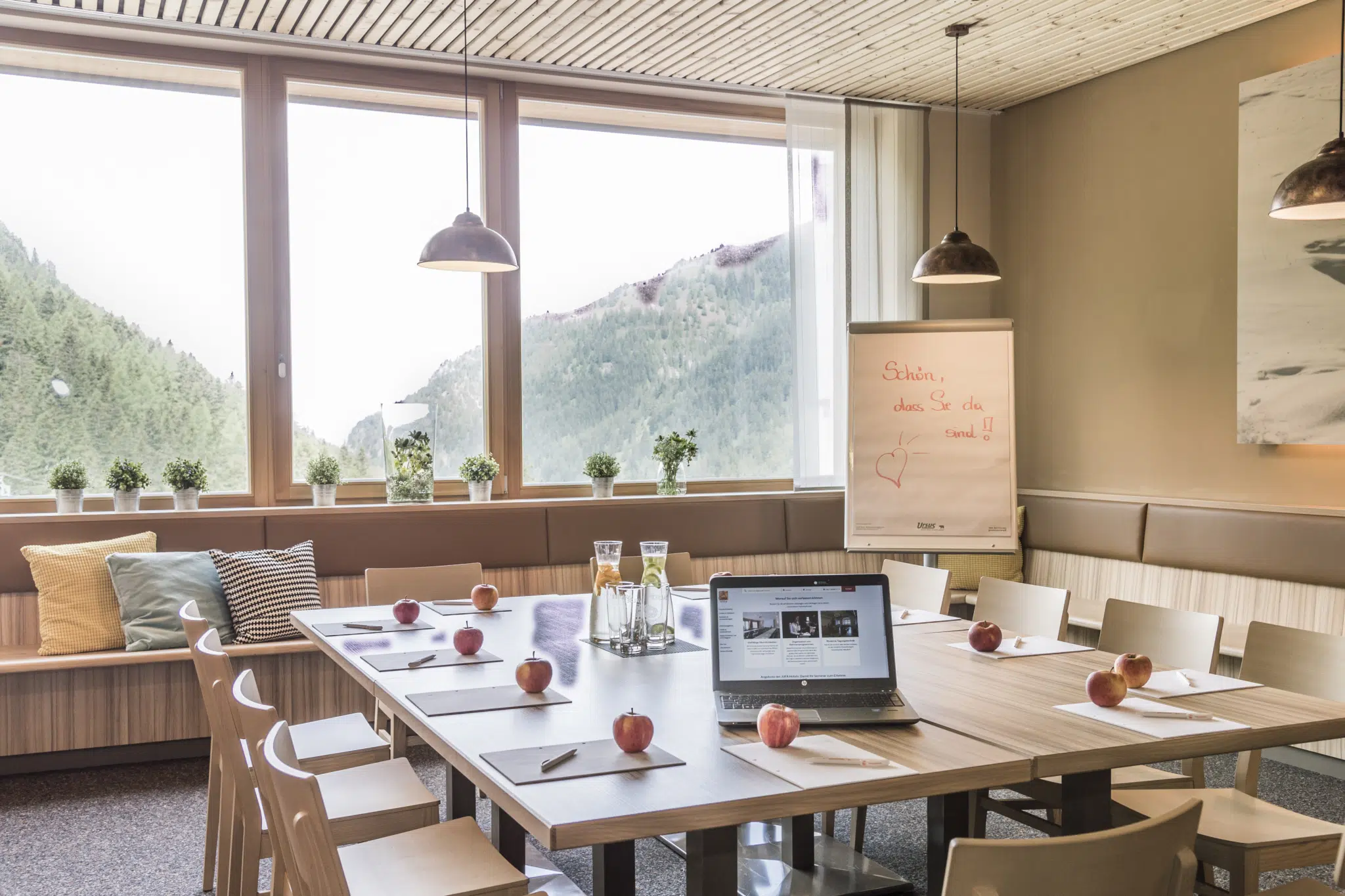 Besprechungstischmit Laptop und Äpfeln im Restaurantbereicht im JUFA Hotel Malbun Alpin-Resort. Der Ort für erholsamen Familienurlaub und einen unvergesslichen Winter- und Wanderurlaub.