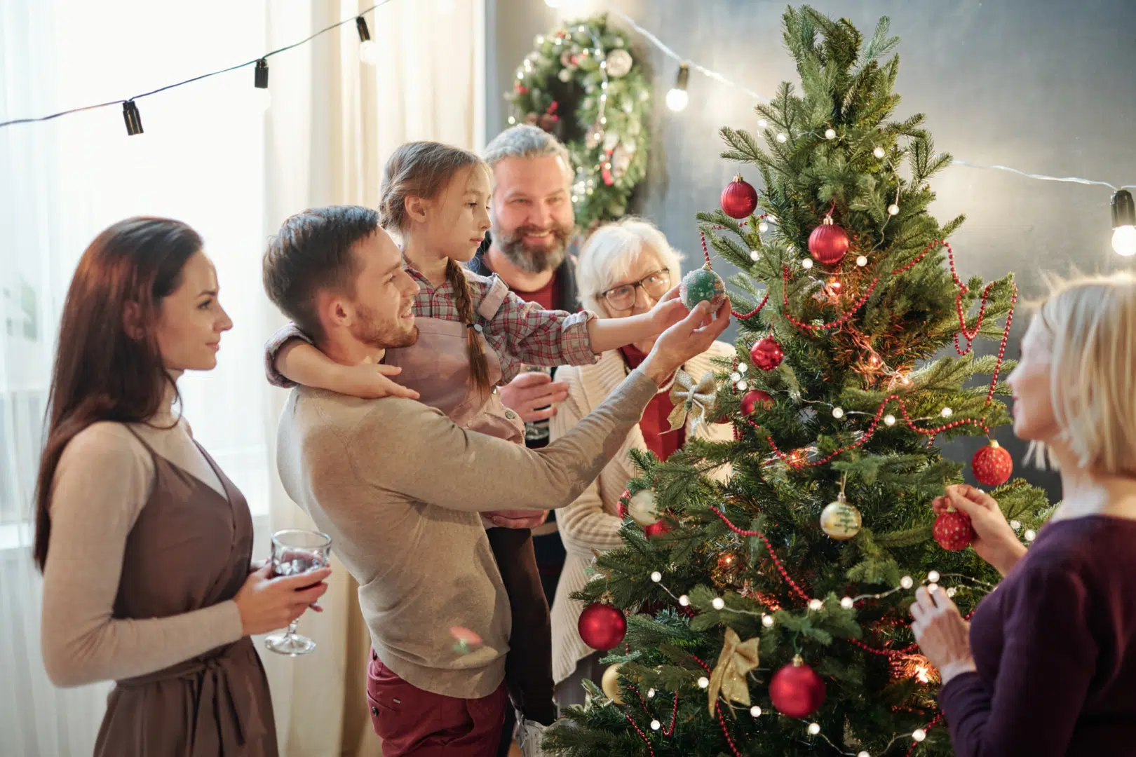 Ihr seht eine Familie mit Eltern, Kind und Großeltern neben einem bunt geschmückten Weihnachtsbaum in der Adventzeit.