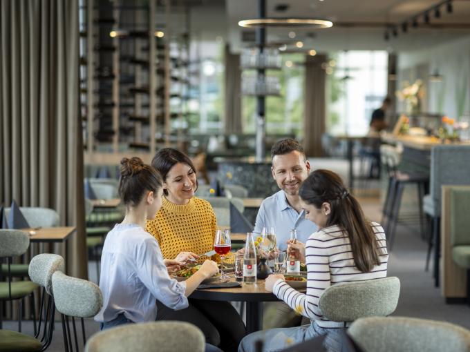 Sie sehen eine vierköpfige Familie beim gemütlichen Mittag- und Abendessen im Café & Restaurant Wandelhalle im JUFA Hotel Bad Radkersburg